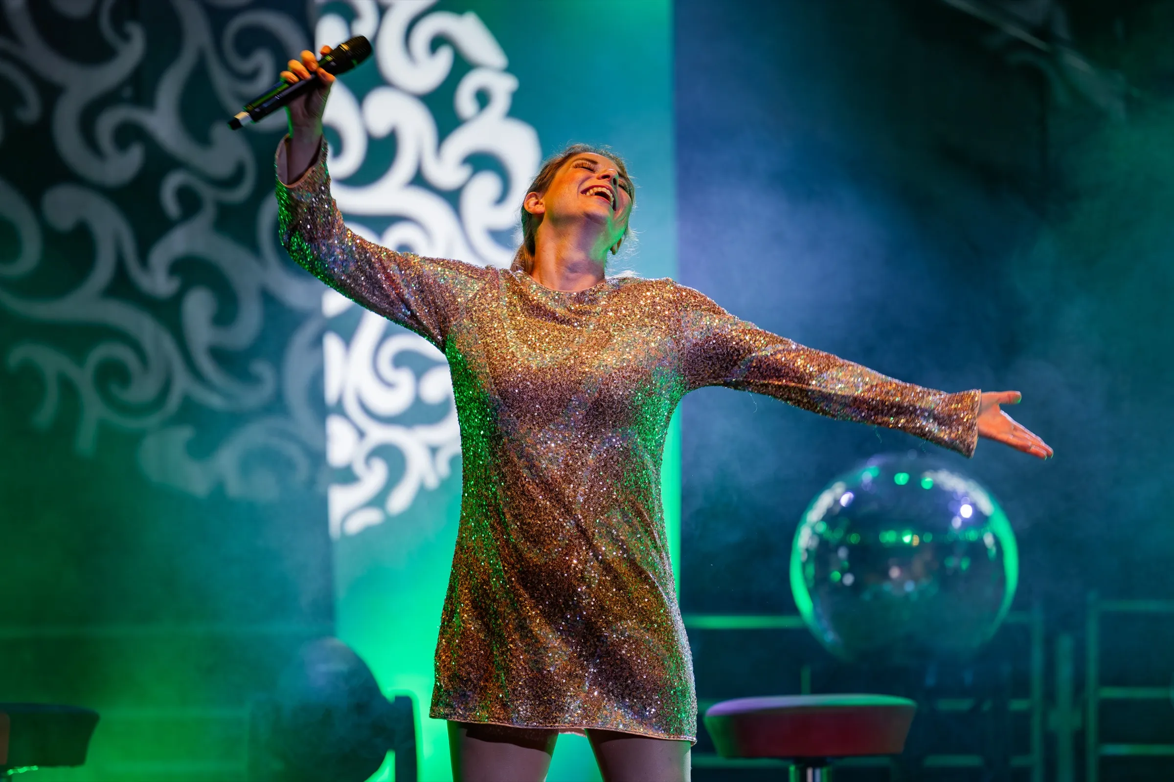 Nicole Behnke singt im goldenen Kleid auf der Bühne, Arme ausgebreitet, grünes Bühnenlicht