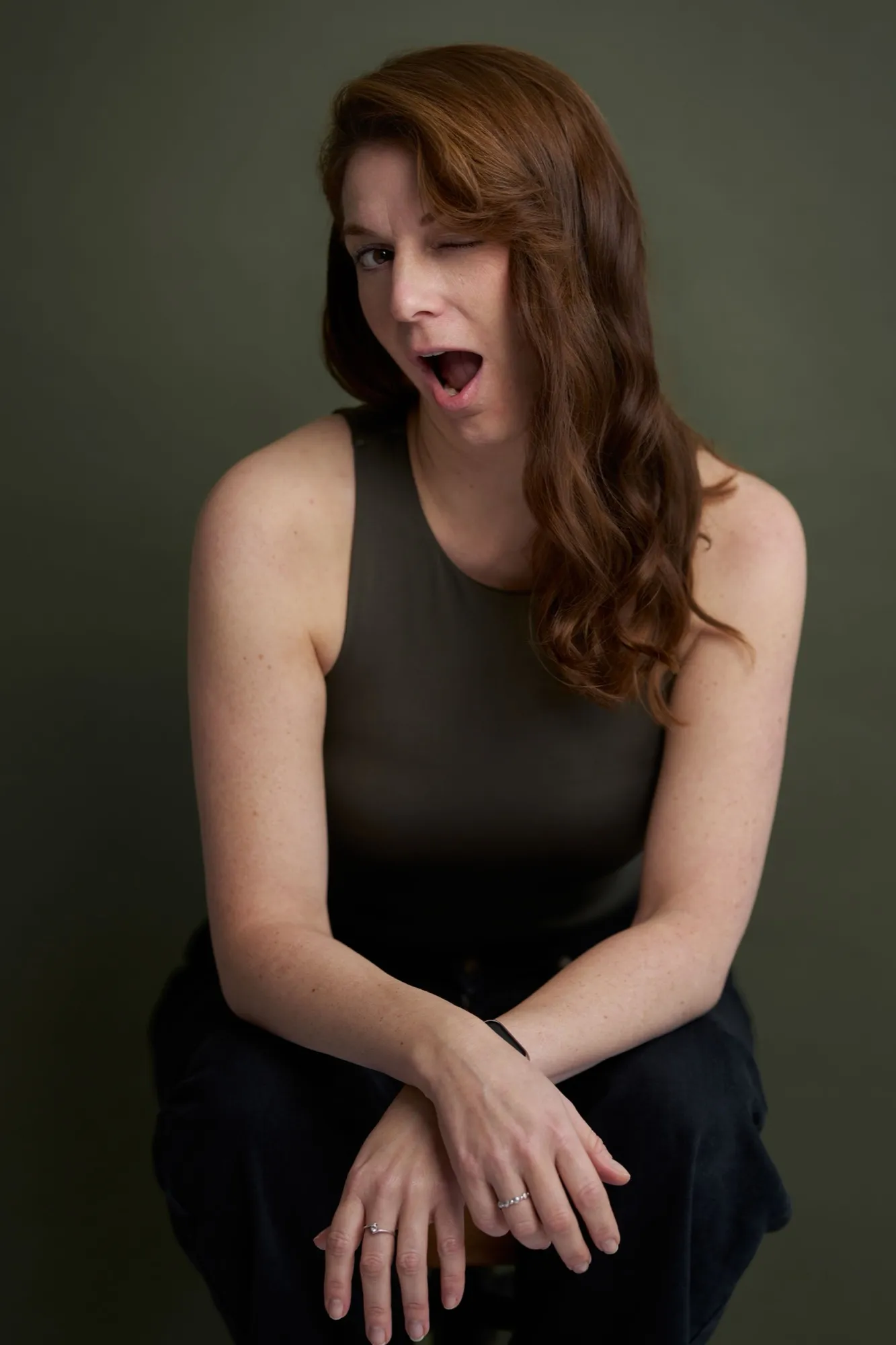Nicole Behnke zwinkert mit weit geöffnetem Mund, expressives Portrait vor moosgrünem Hintergrund