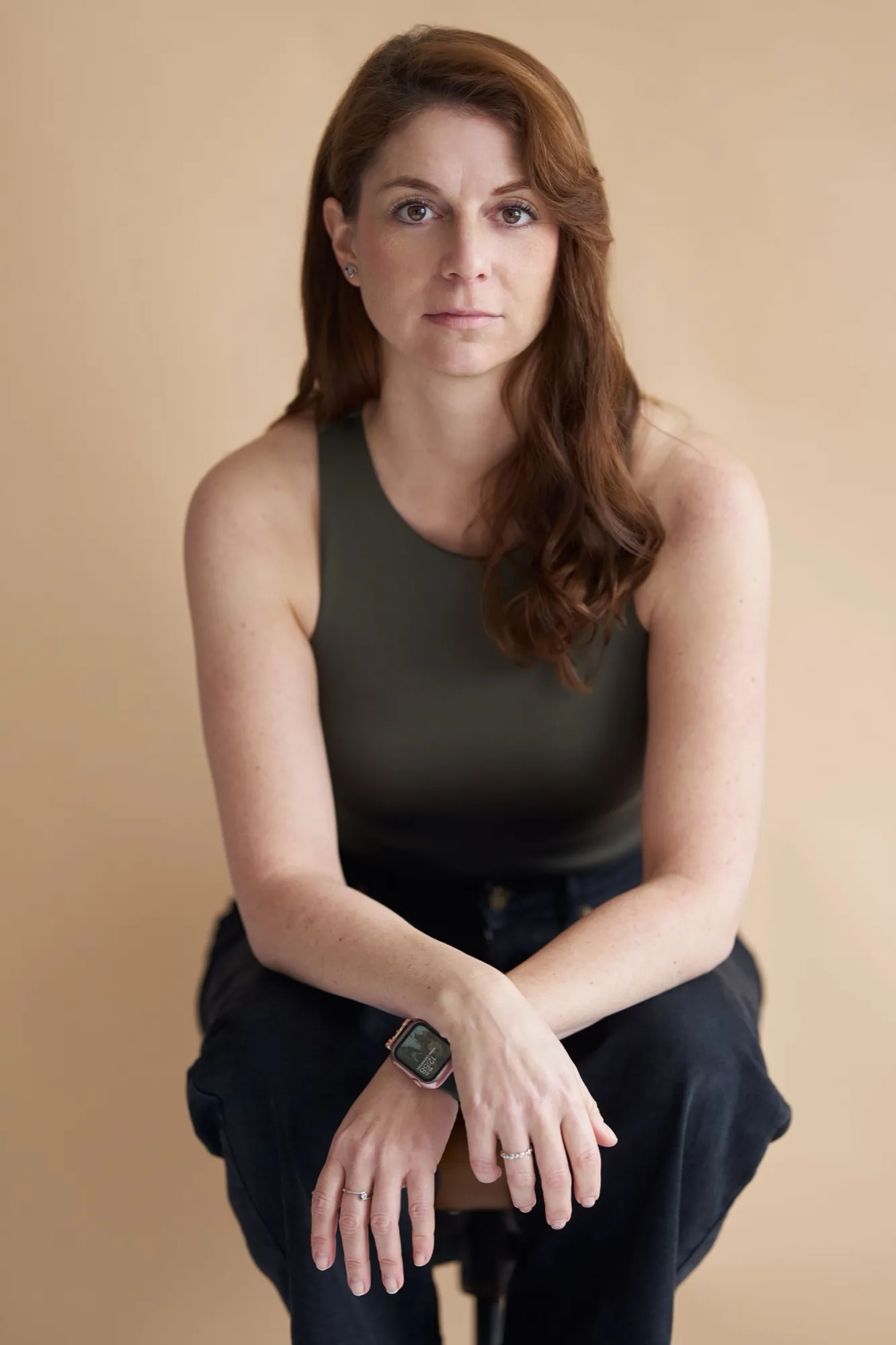 Portrait von Nicole Behnke, auf einem Hocker sitzend vor sandfarbenem Hintergrund
